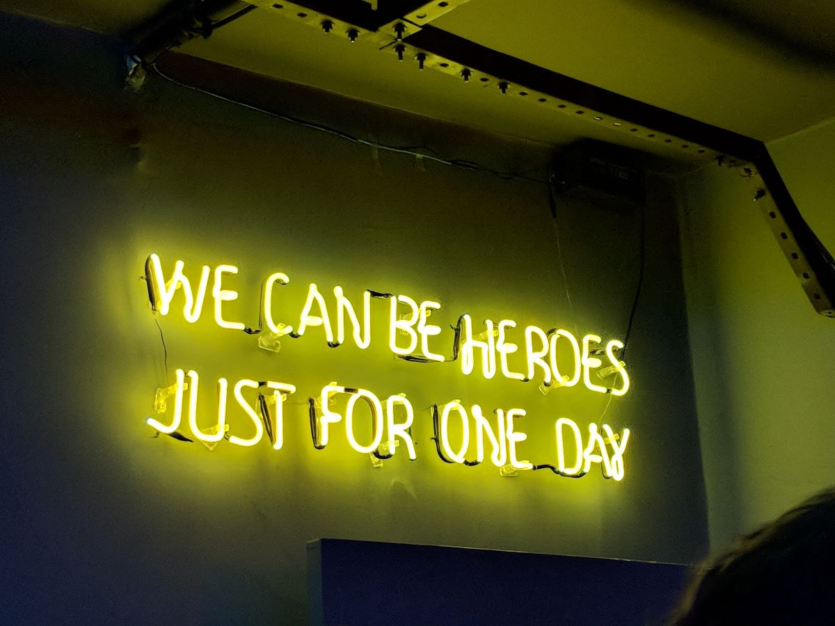 A neon sign that says "We can be heroes just for one day"