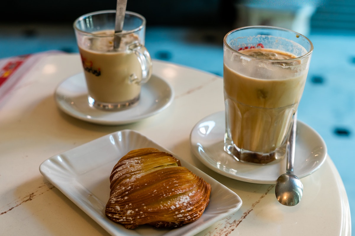 A table with two clear classes of iced coffee and a classic sfogliatella pastry on a plate.