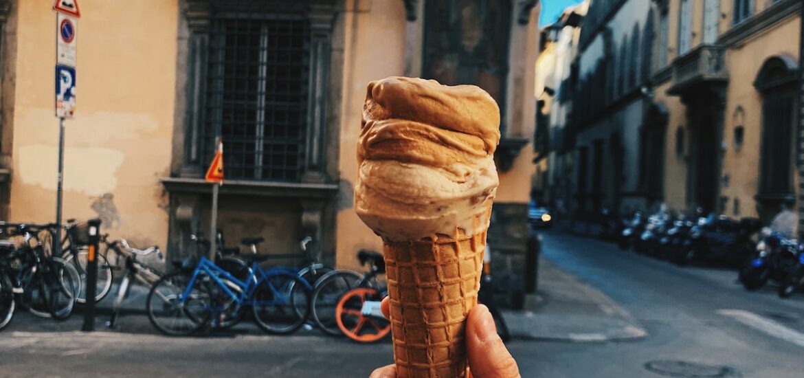 Person's hand holding up a gelato cone in front of a building