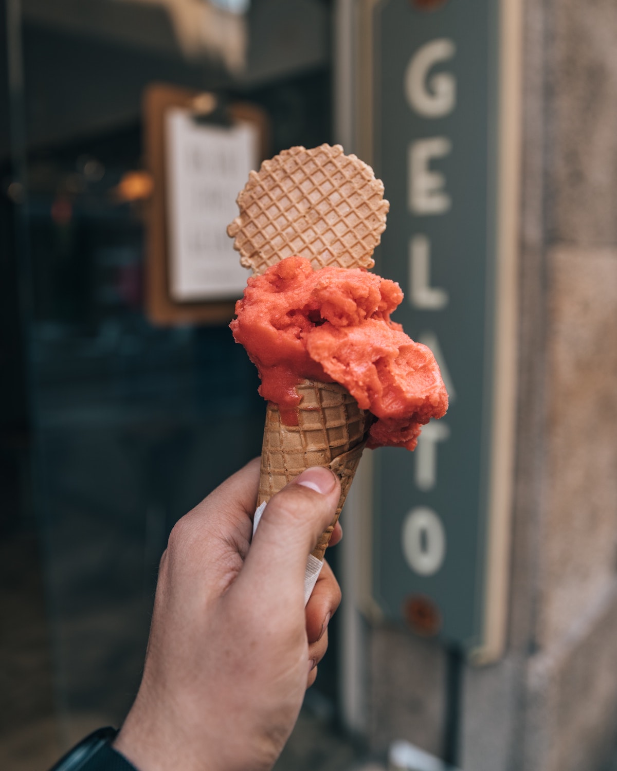 Person's hand holding a cone of red gelato with a wafer stuck into the top