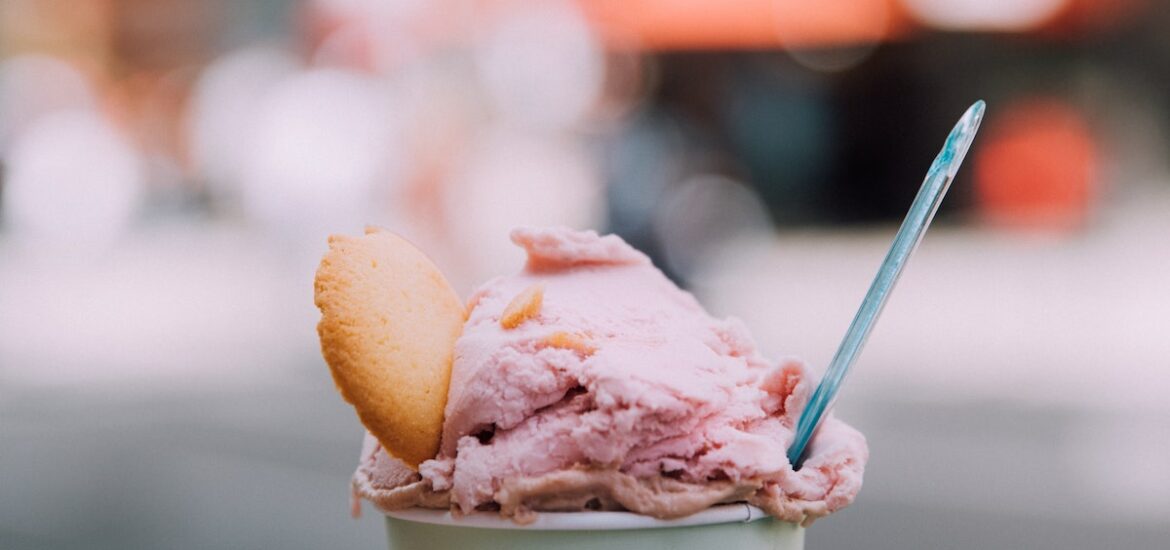 Person's hand holding a small cup of pink gelato garnished with a cookie