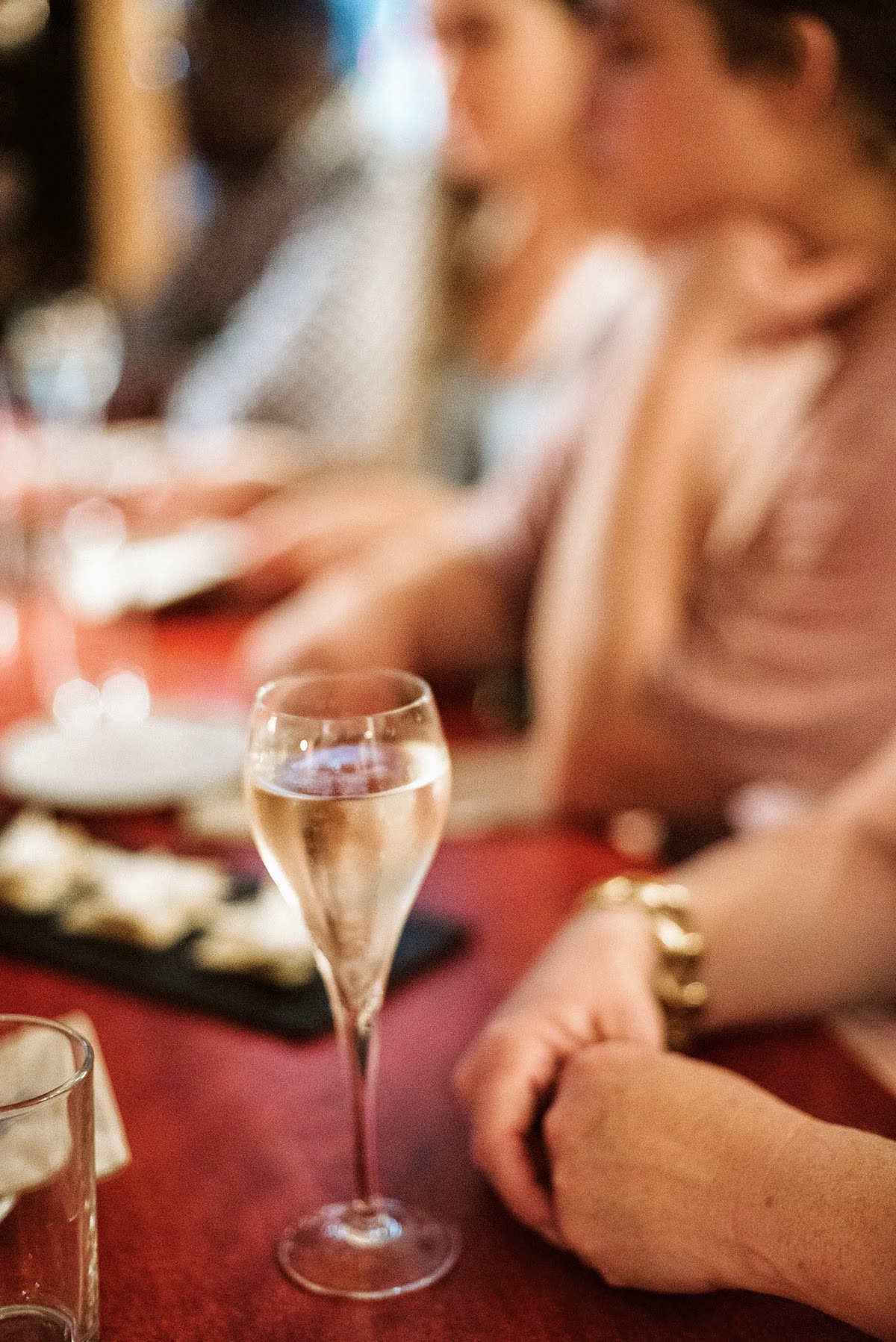 Glass of sparkling wine on a red table surrounded by people and other dishes