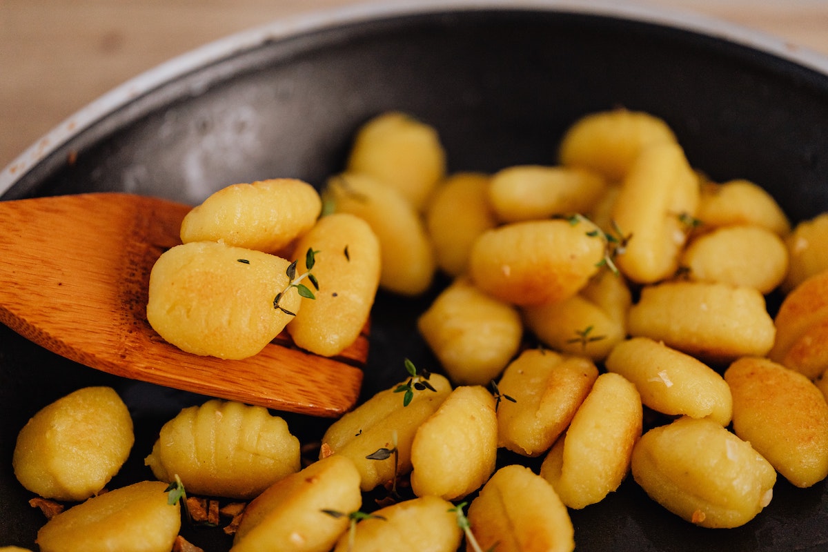 Gnocchi garnished with herbs in a frying pan with a wooden spatula
