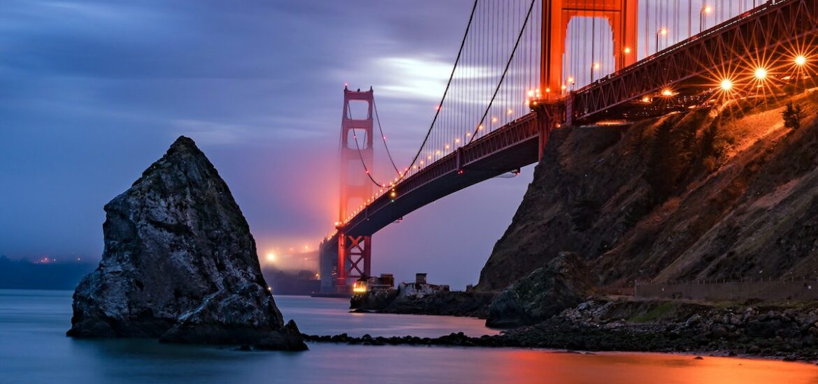 The Golden Gate Bridge at dusk with fog rolling in an the lights reflecting off the San Francisco bay.