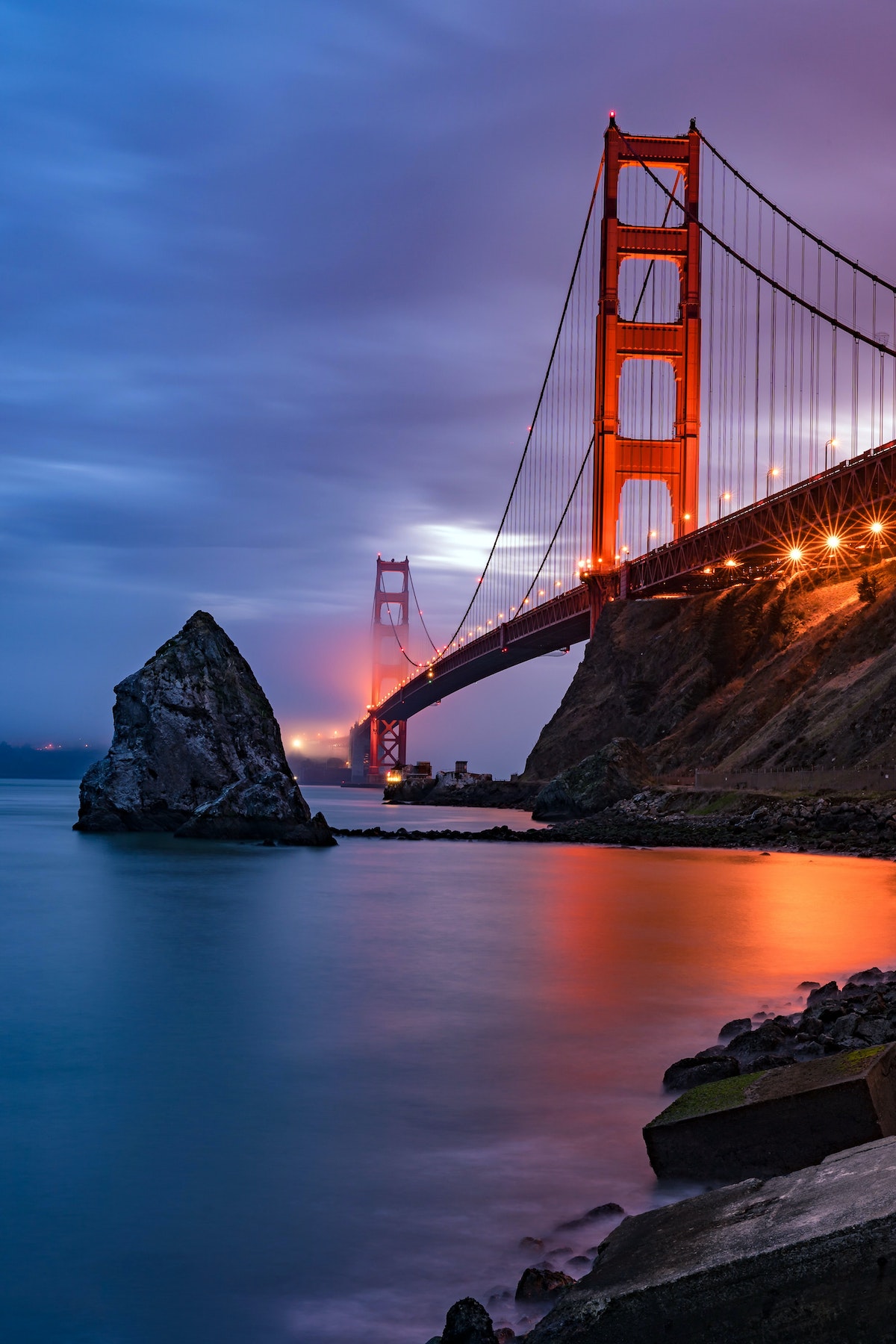 The Golden Gate Bridge at dusk with fog rolling in an the lights reflecting off the San Francisco bay.
