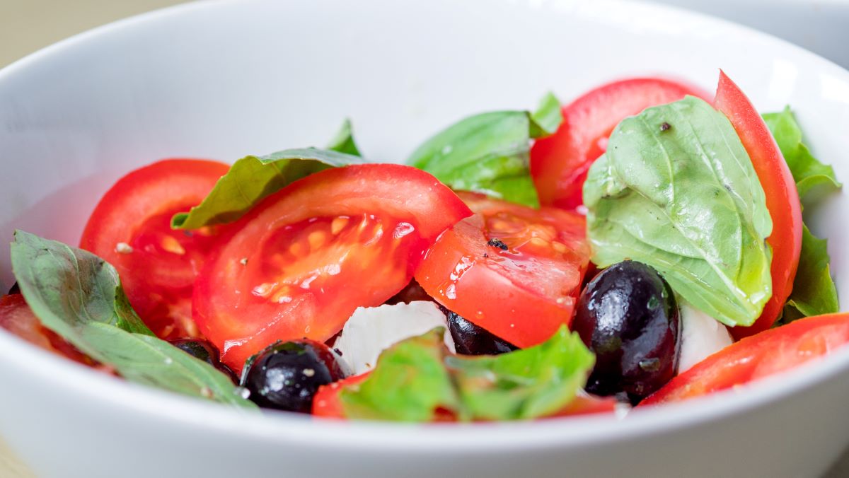 A tomato, basil, olive and mozzerella salad in a small bowl
