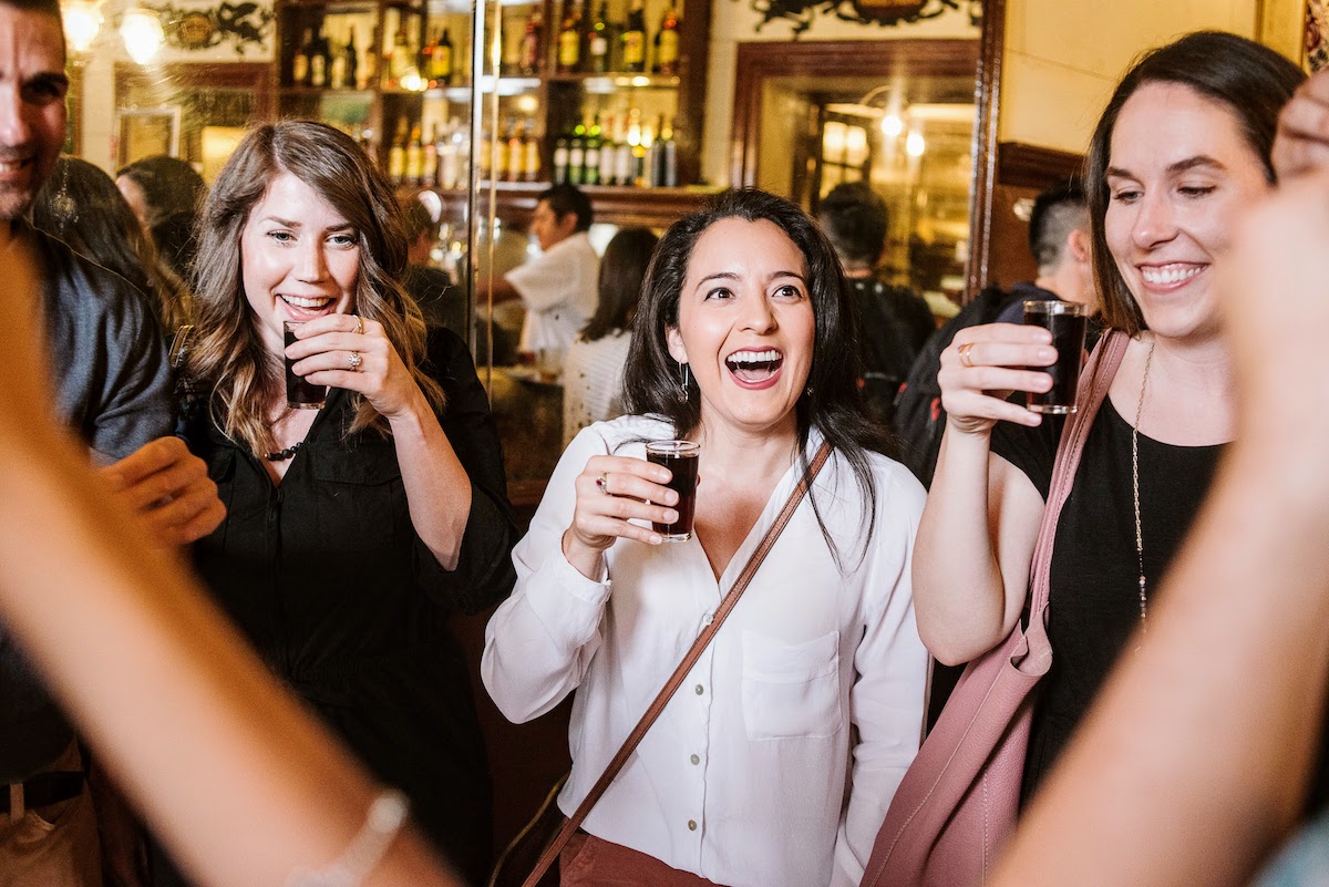 Three women smiling and drinking small glasses of vermouth