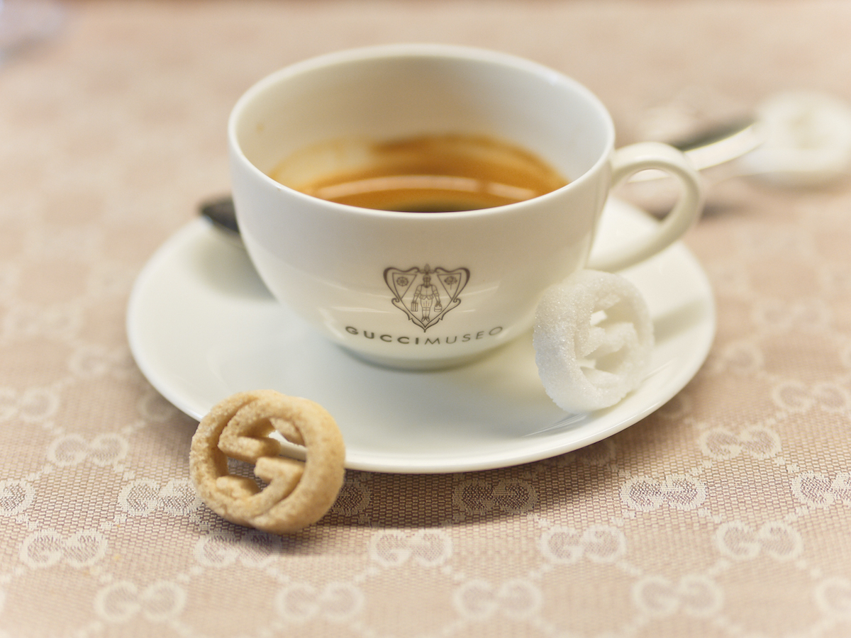Small cup of espresso served in a porcelain mug with the emblem "Gucci Museo" with one white and one brown sugar cube in the shape of 2 interlocking Gs