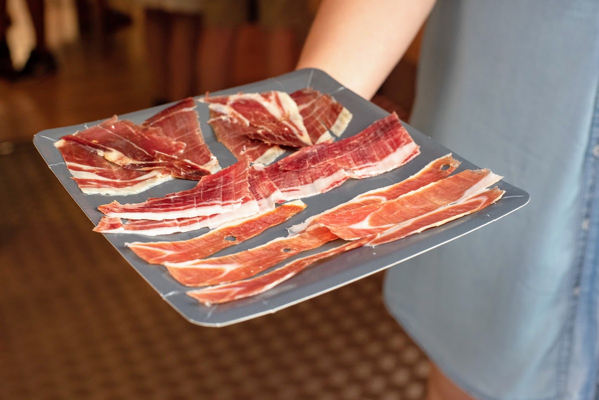 Person's hand holding a tray of cured ham.