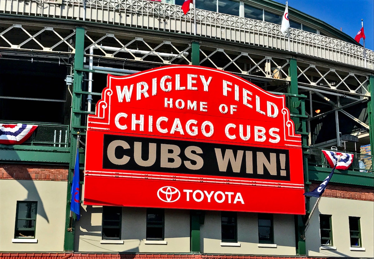 A big red sign reads "Wrigly Field Home of Chicago Cubs" in white letters. LED lights beneath read "CUBS WIN!" Going to a Cubs game is a great thing to do in Chicago with kids.