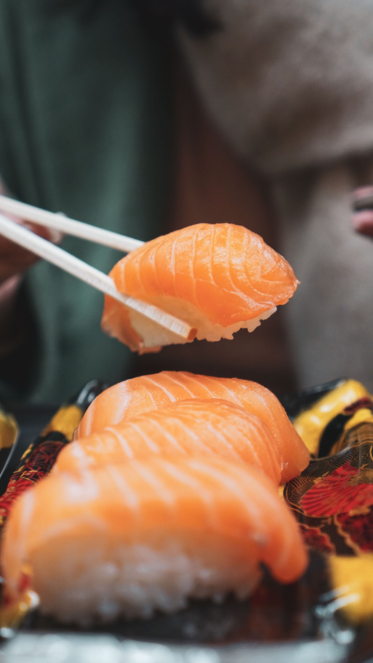 close up of a person picking up a sushi roll with chopsticks