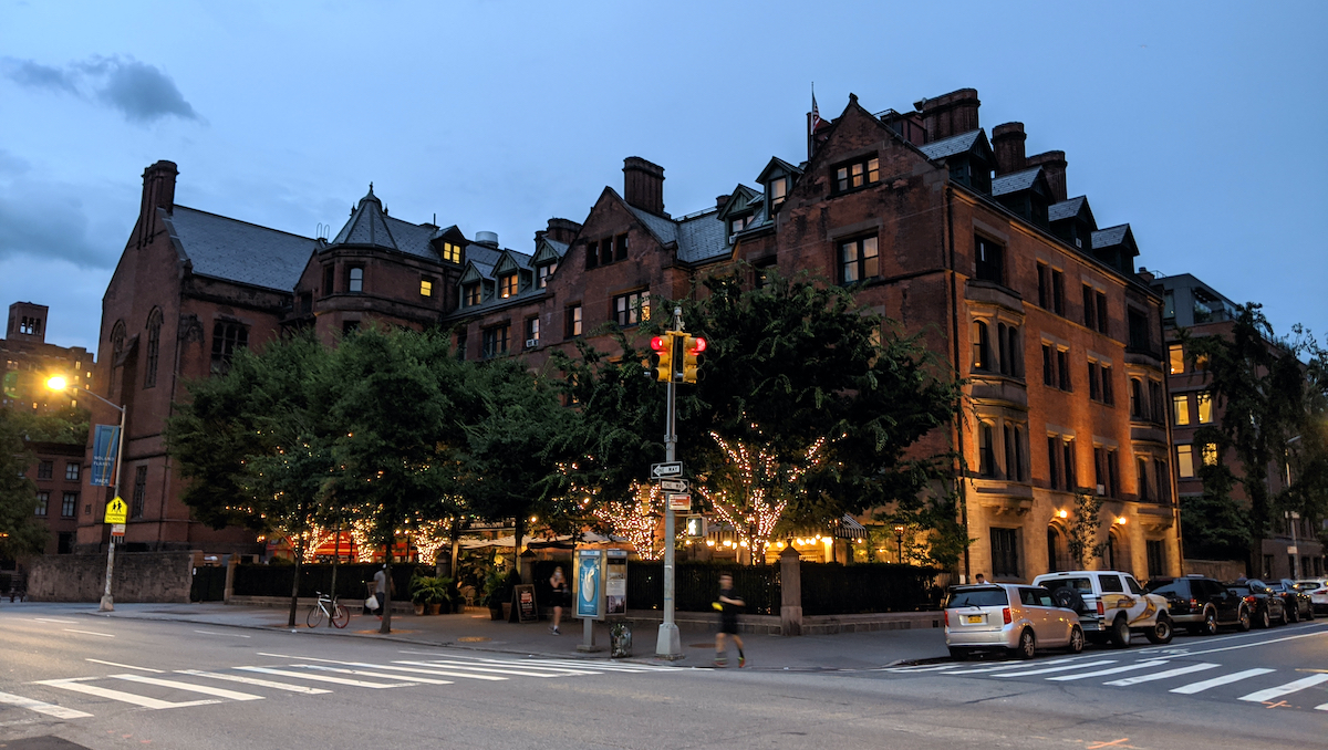 Exterior of a multi story brick historic building at dusk with string lights in the trees outside