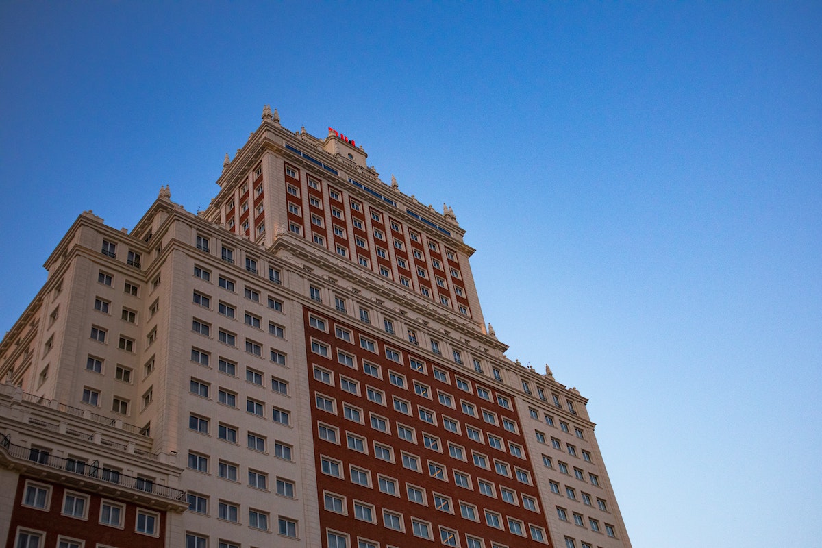 Upward view of a large beige and red brick hotel building against a clear blue sky.