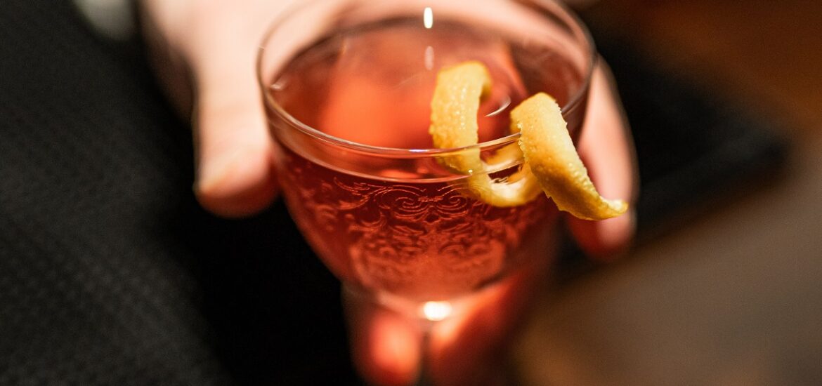 Bar tender handing out an elegant cocktail class filled with orange liquid in a dark club, bar, or speakeasy