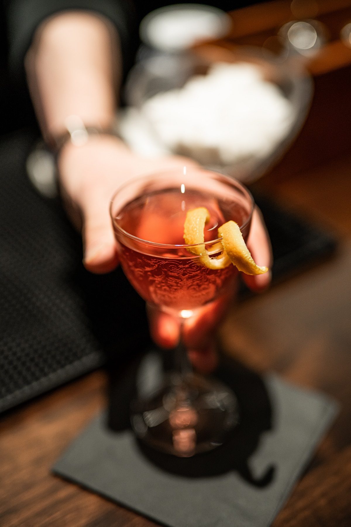 Bar tender handing out an elegant cocktail class filled with orange liquid in a dark club, bar, or speakeasy