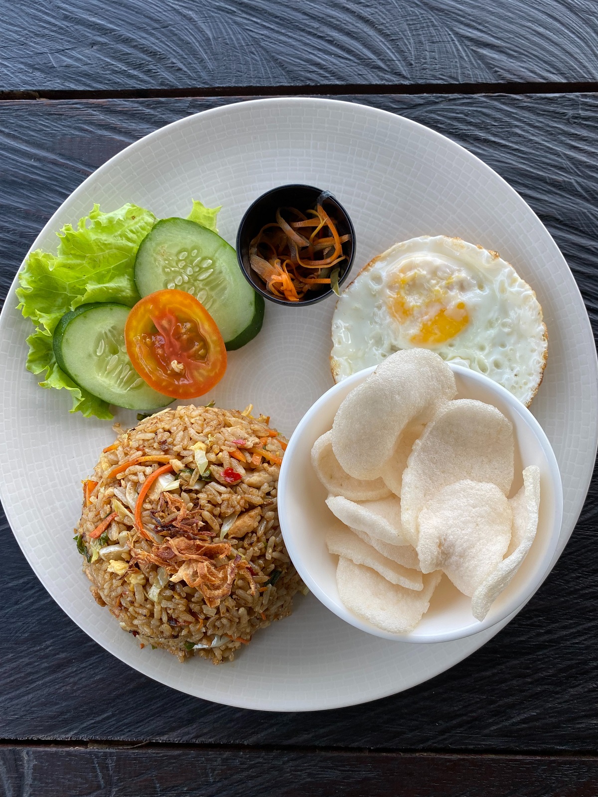 Nasi goreng, a rice dish with vegetables, a fried egg, and fresh cucumber