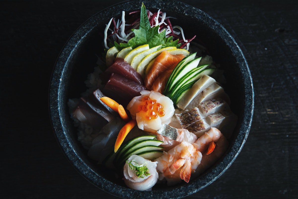 A black bowl atop a black table filled with sushi ingredients 