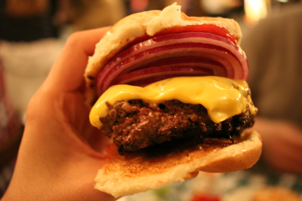 Person's hand holding a cheeseburger with red onion.
