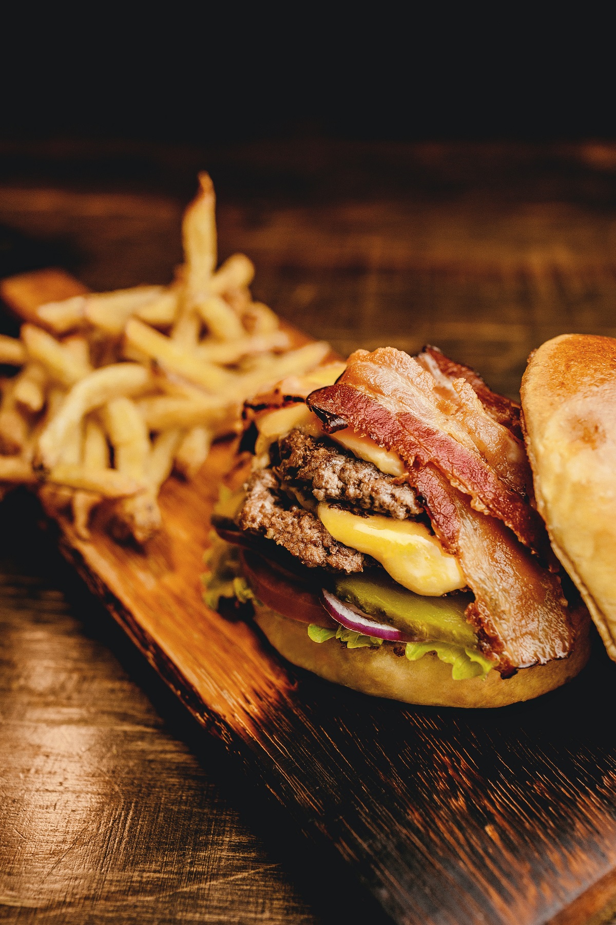 Cheeseburger with pickles and bacon served on a wooden plate with fries