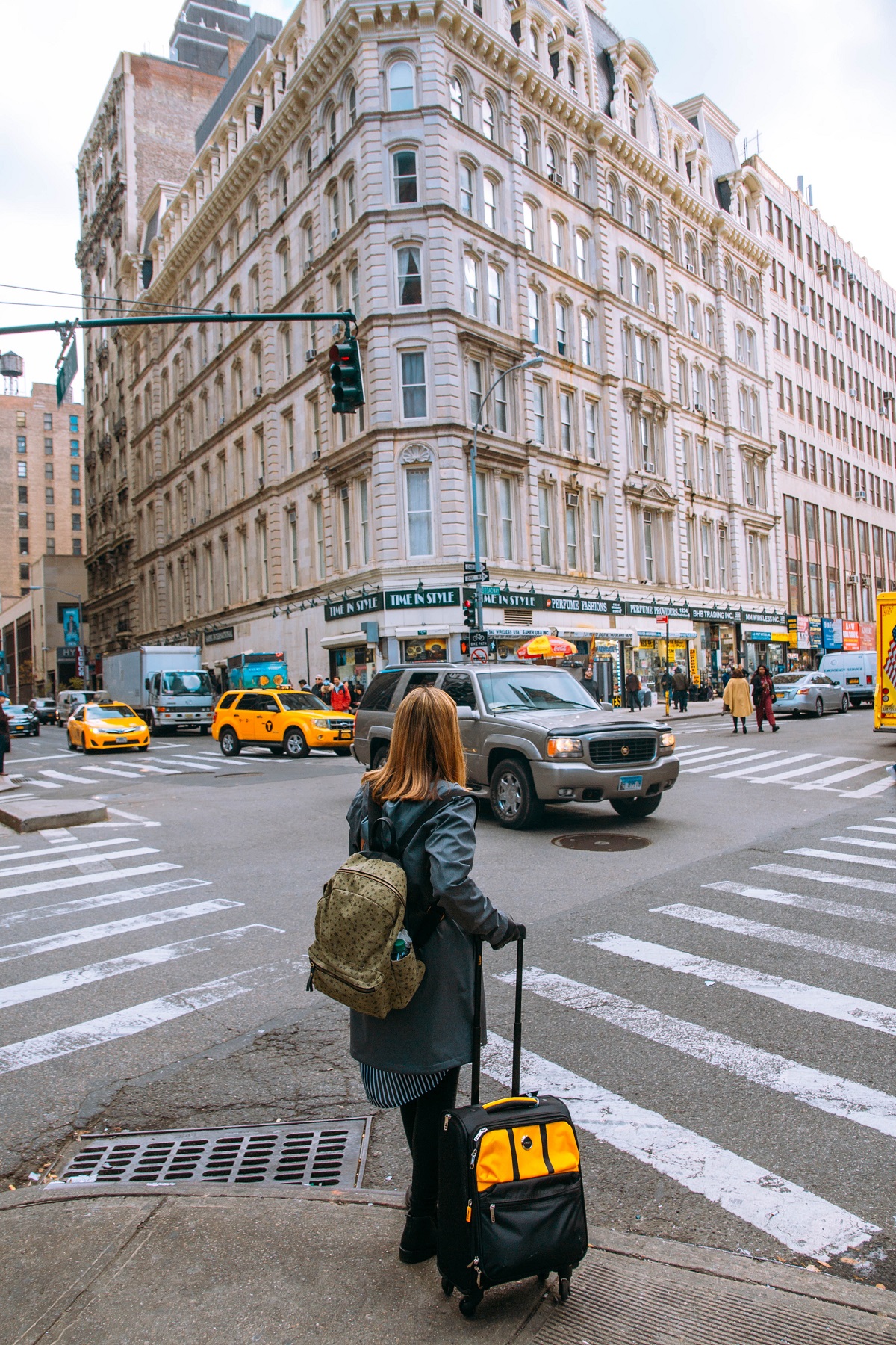 A woman with a suitcase waits at a busy crosswalk in the middle of a city