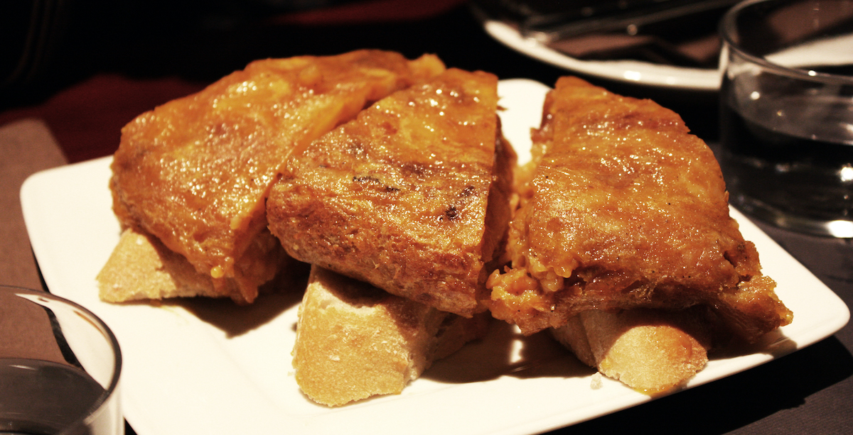 Three pieces of Spanish potato omelet, each atop a small slice of bread on a white plate