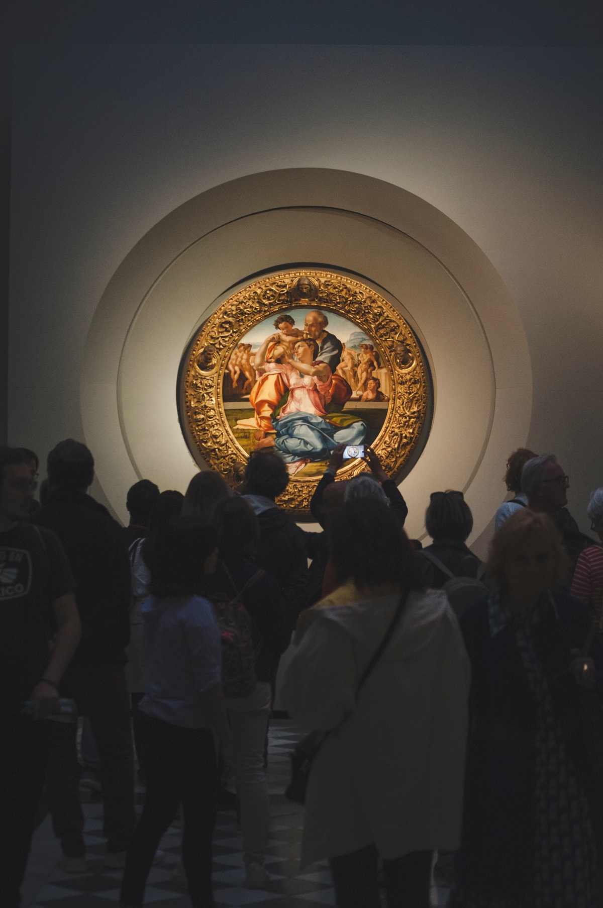Visitors in a dark art museum gather around a painting illuminated by lights