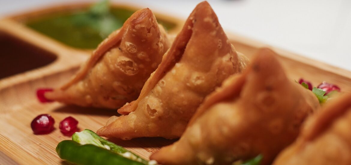 Wooden plate of three small triangular samosas and green peppers