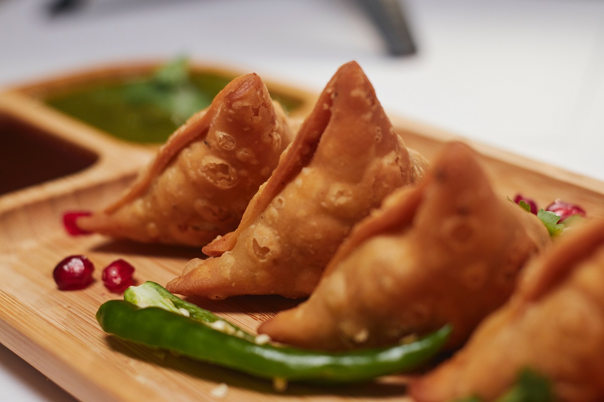 Wooden plate of three small triangular samosas and green peppers