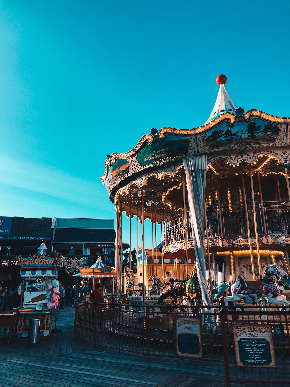 View of a retro carousel and churro stand with restaurants behind at San Francisco's Pier 39.