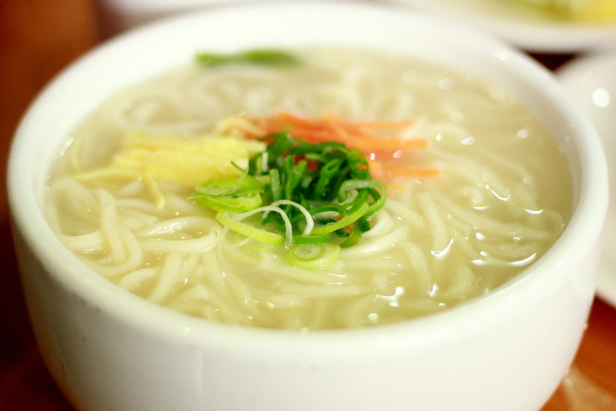 Korean noodle soup garnished with chives and sliced carrots