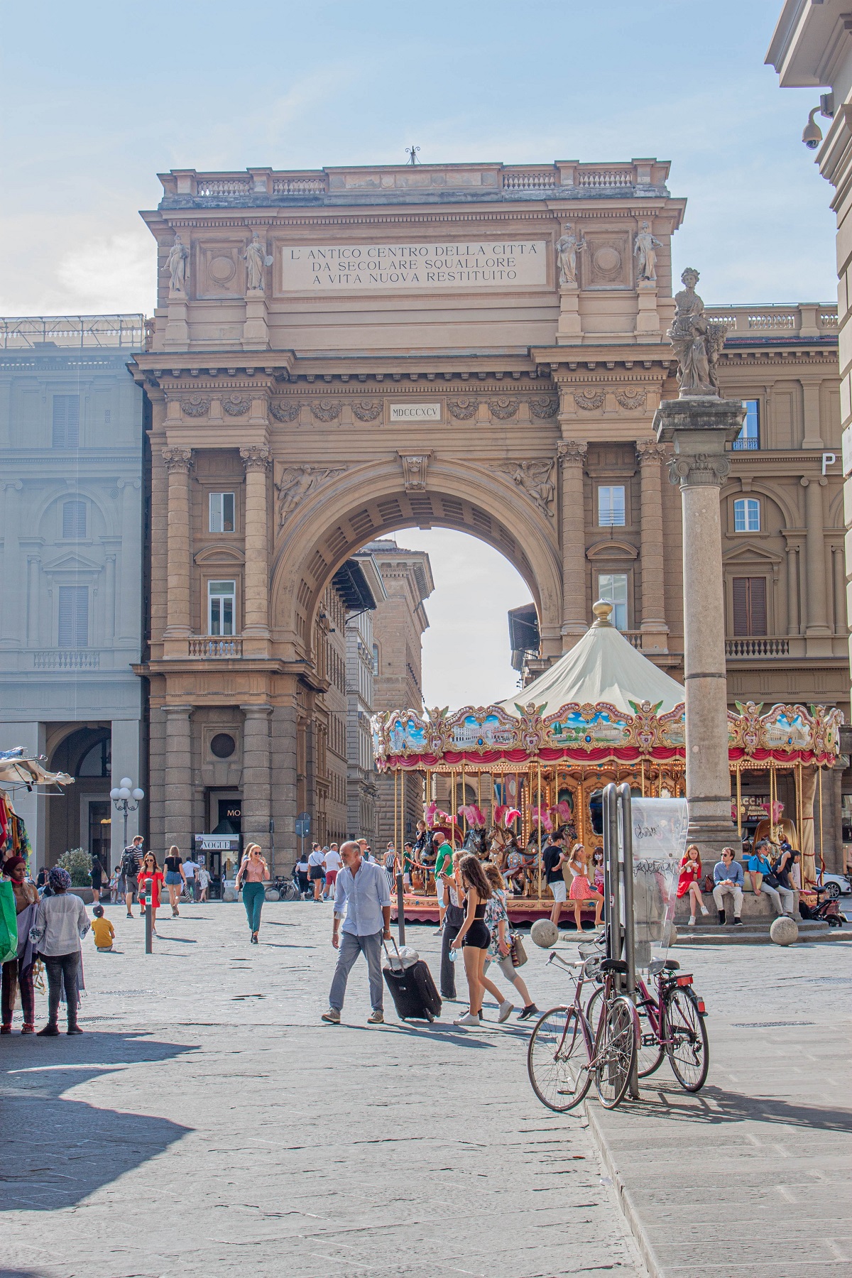 Tourists in Florence drag their suitcases across a famous piazza in Italy with bikes near them