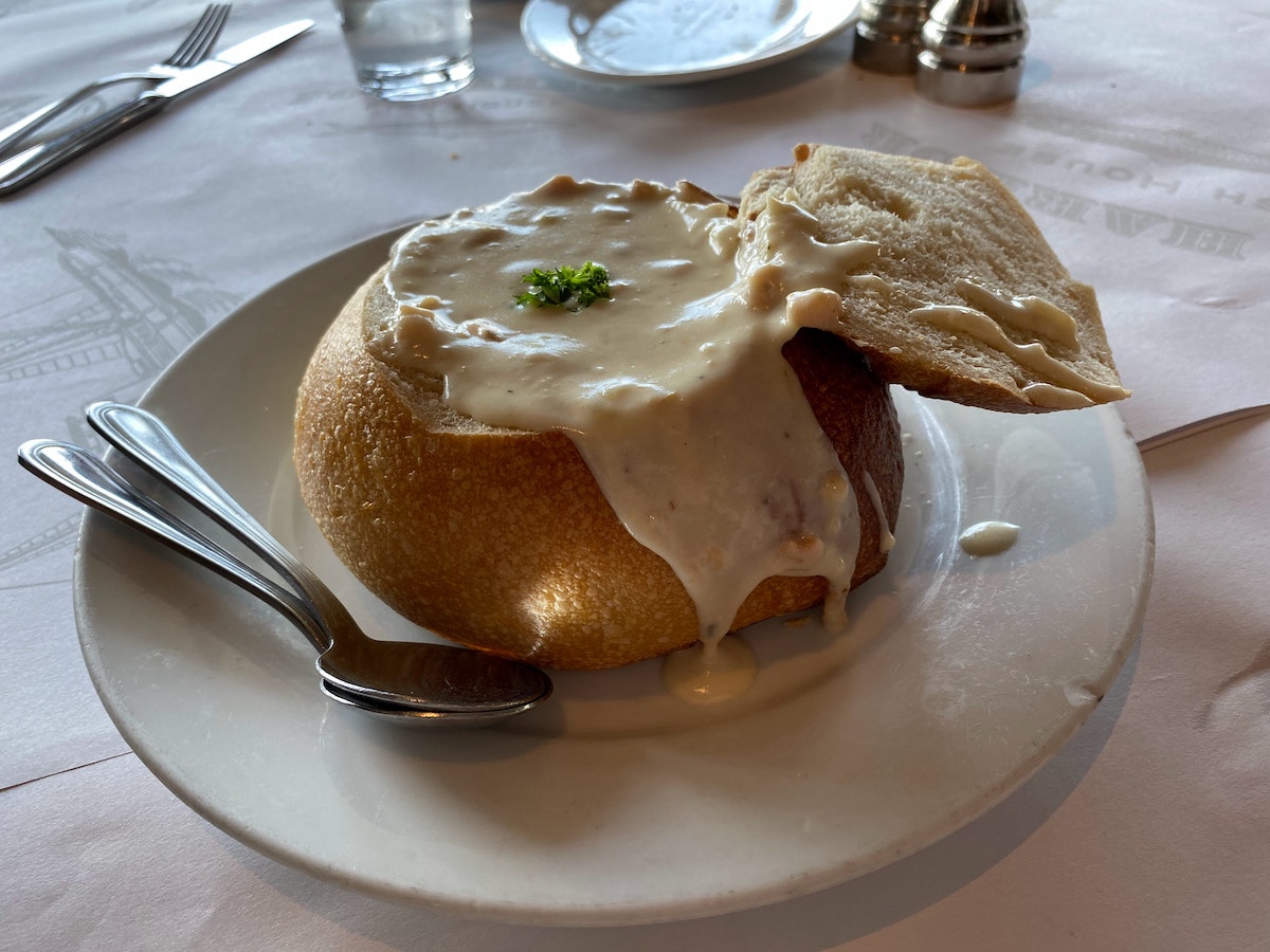 A sourdough bread bowl filled with white clam chowder on a white plate. A classic dish to try on San Francisco's Pier 39.