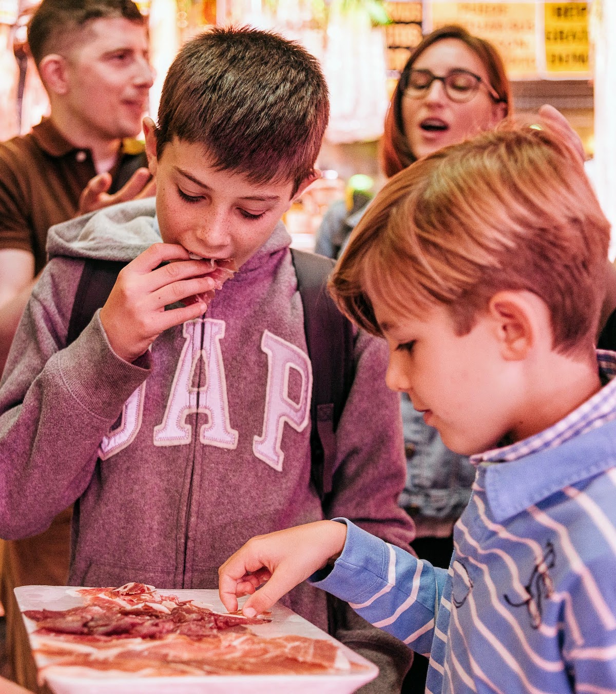Two boys eating Spanish cured ham off of a white tray