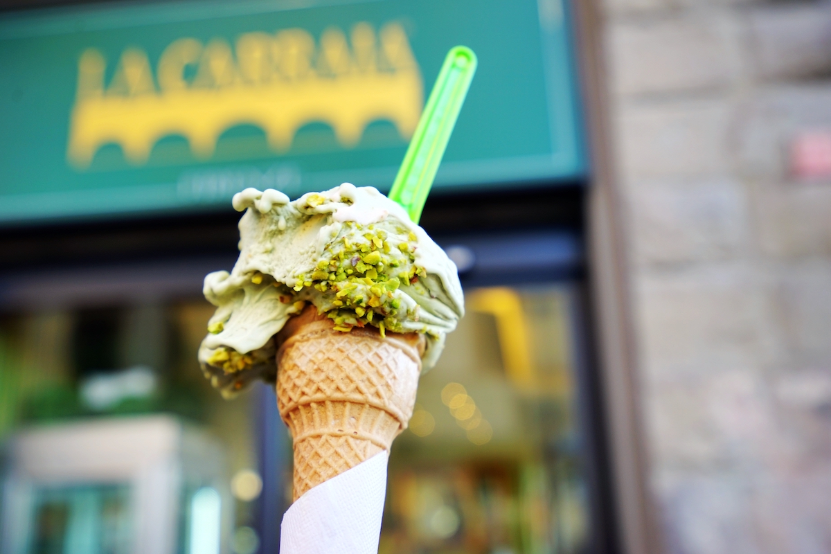 Pistachio gelato in a cone being held up in front of a green awning