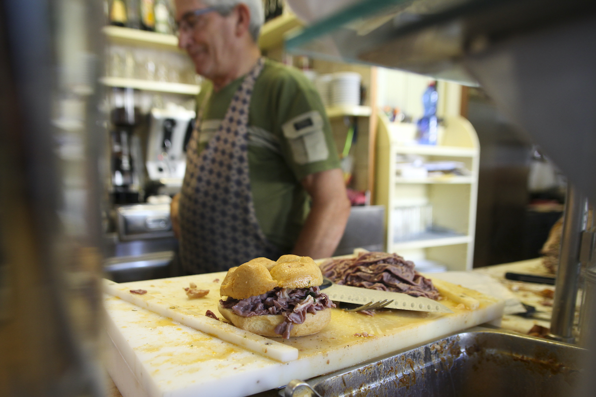 Tripe sandwich on a deli counter with a man wearing an apron in the background