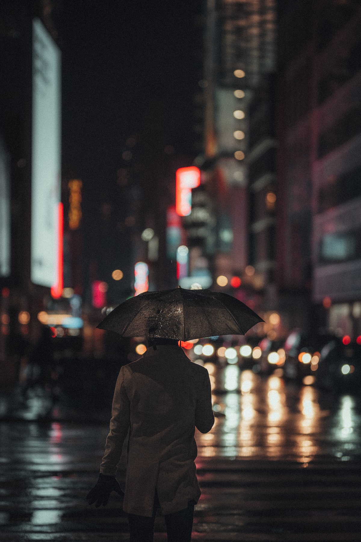 Person walks with an umbrella on a rainy street in a busy city at night