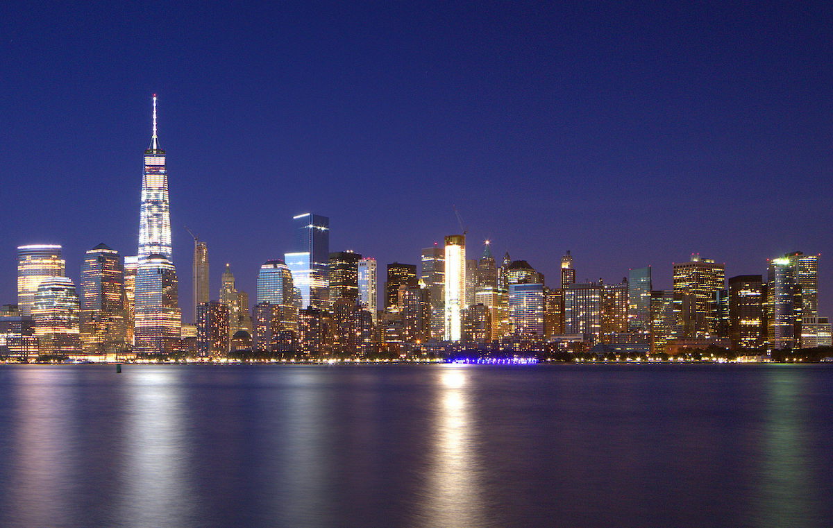 New York City skyline lit up at night as seen from across a body of water.
