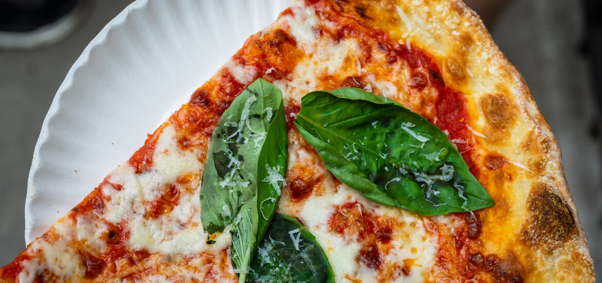 Slice of New York-style pizza topped with fresh basil leaves