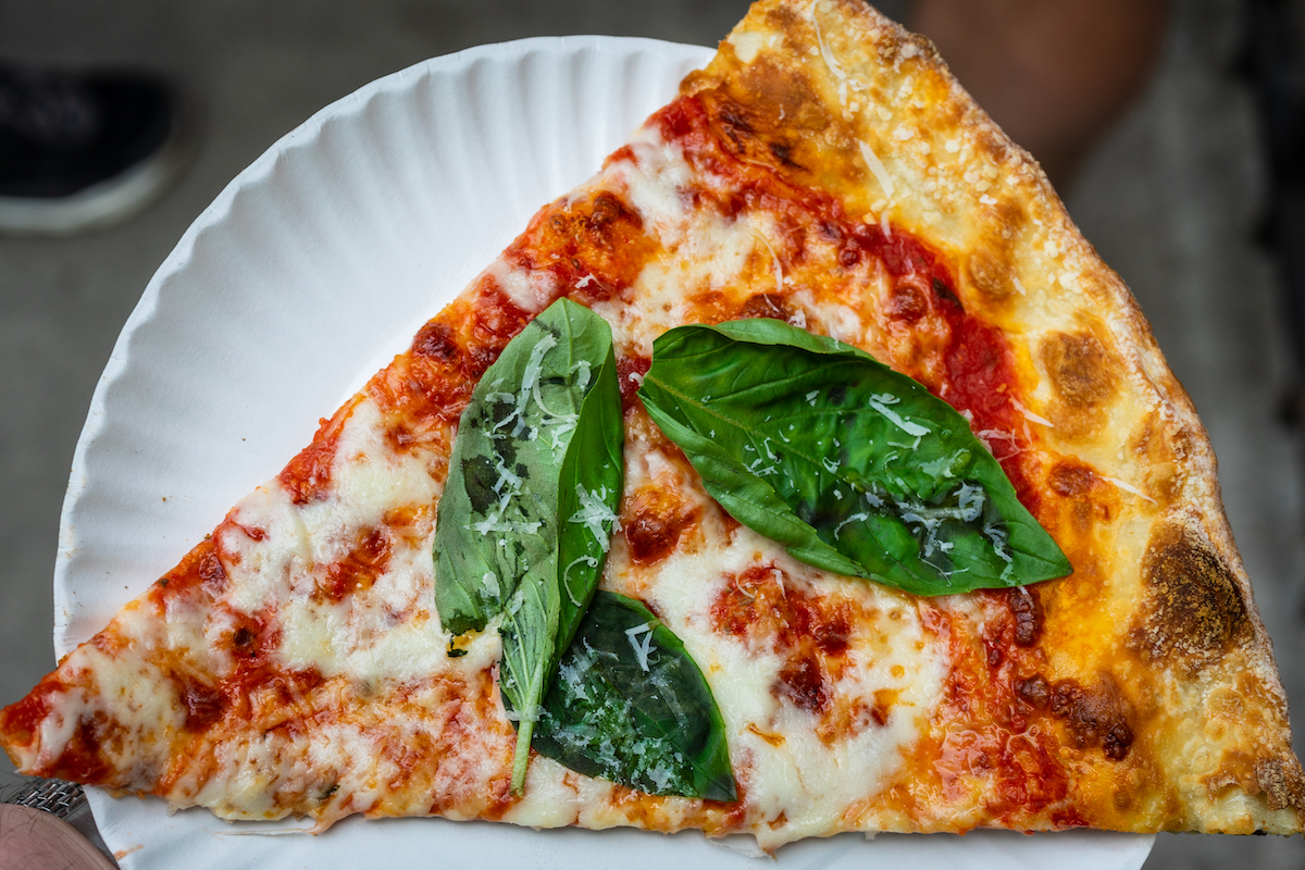 Slice of New York-style pizza topped with fresh basil leaves