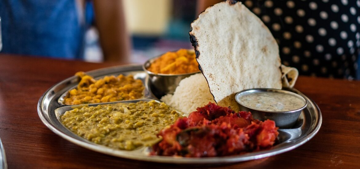 Silver tray of Indian food wiht many colored curries and white bread