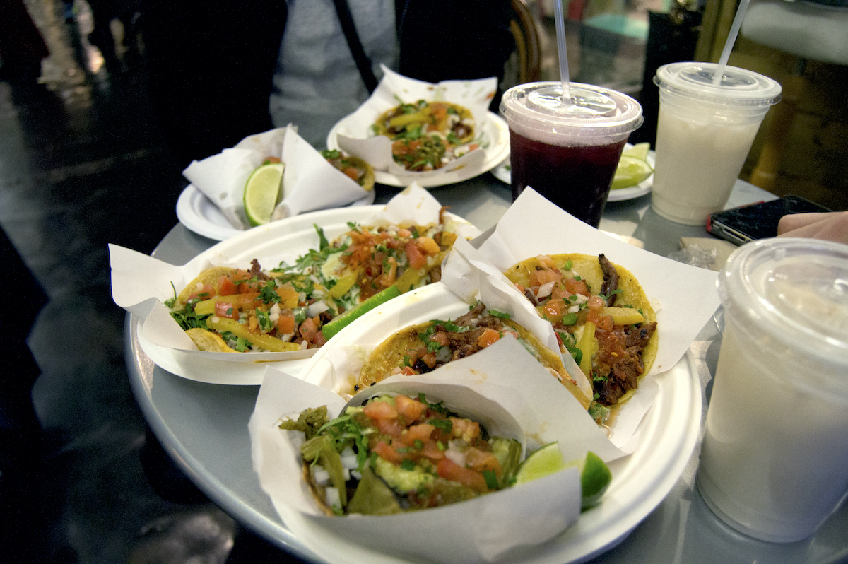 Tacos served on paper plates with an assortment of drinks in plastic cups nearby