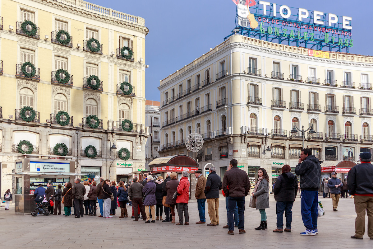 People lining up outside a booth to buy lottery tickets in a large urban plaza