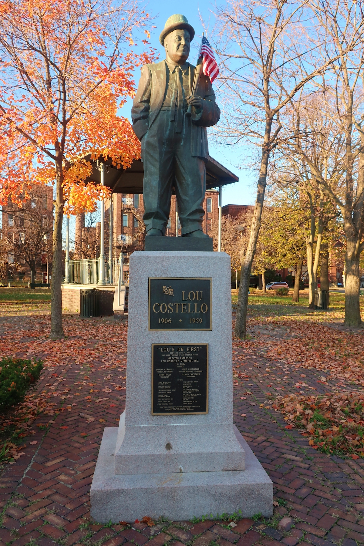 Statue of a man with a real American flag in his hand, seen in a park on a fall day