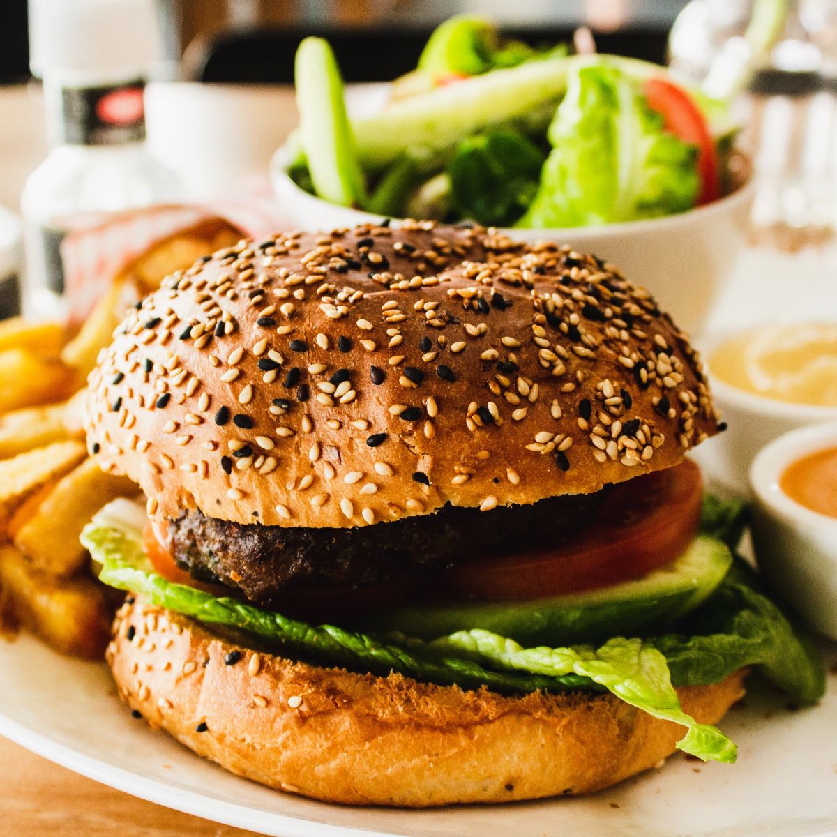 A veggie burge surrounded by a salad and a plate of fries.