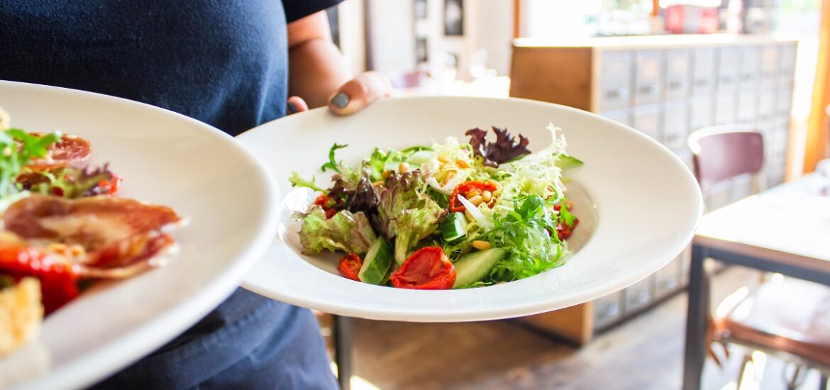 Waiter or waitress brings two white dishes of green salads to a table