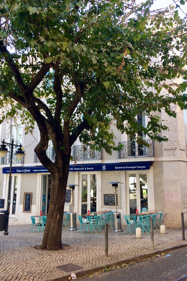 Square with benches and trees in front of a tiled building at The Triangle in Lisbon.