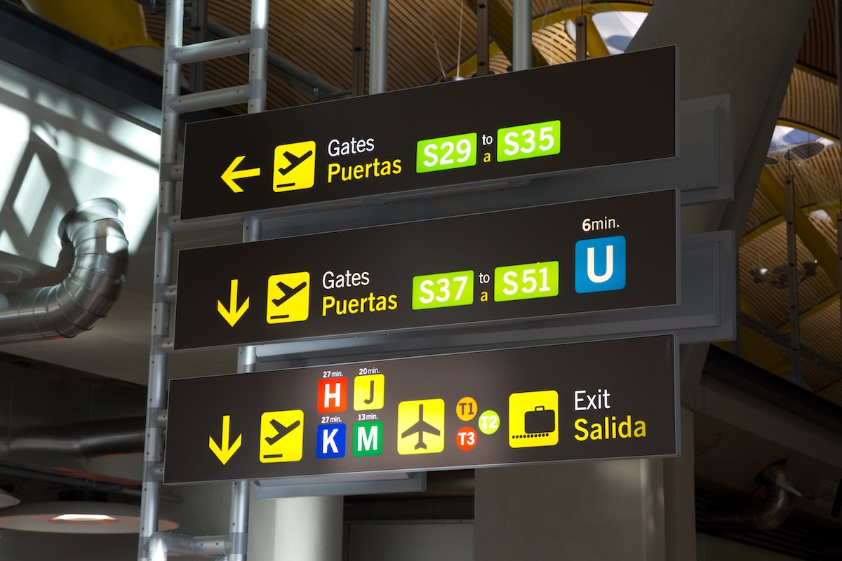 Signs in English and Spanish at the Madrid airport indicating the way to various gates and terminals.