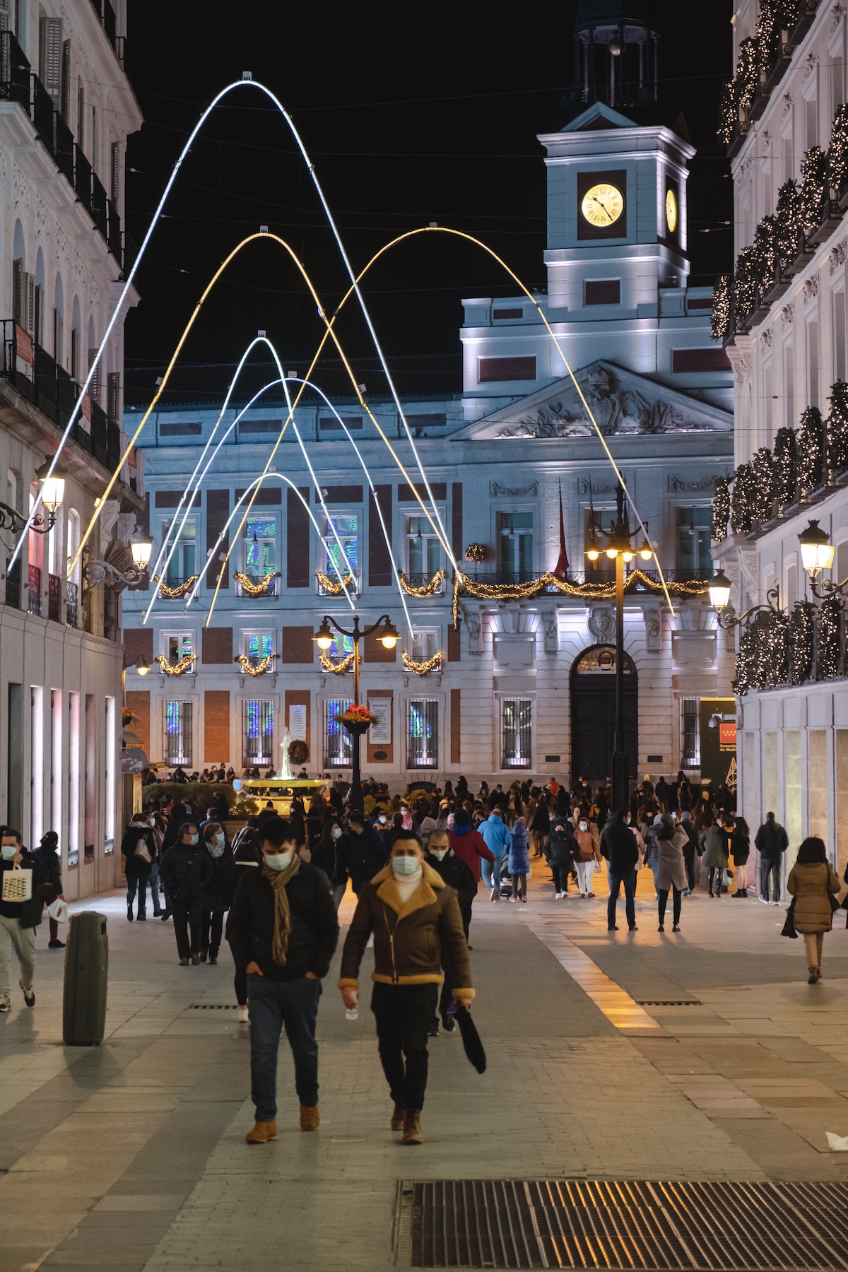 People walking along a city street at night below arched christmas light displays.