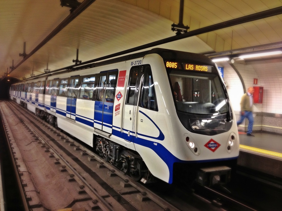 A white and blue train of the Madrid metro arriving at a station.