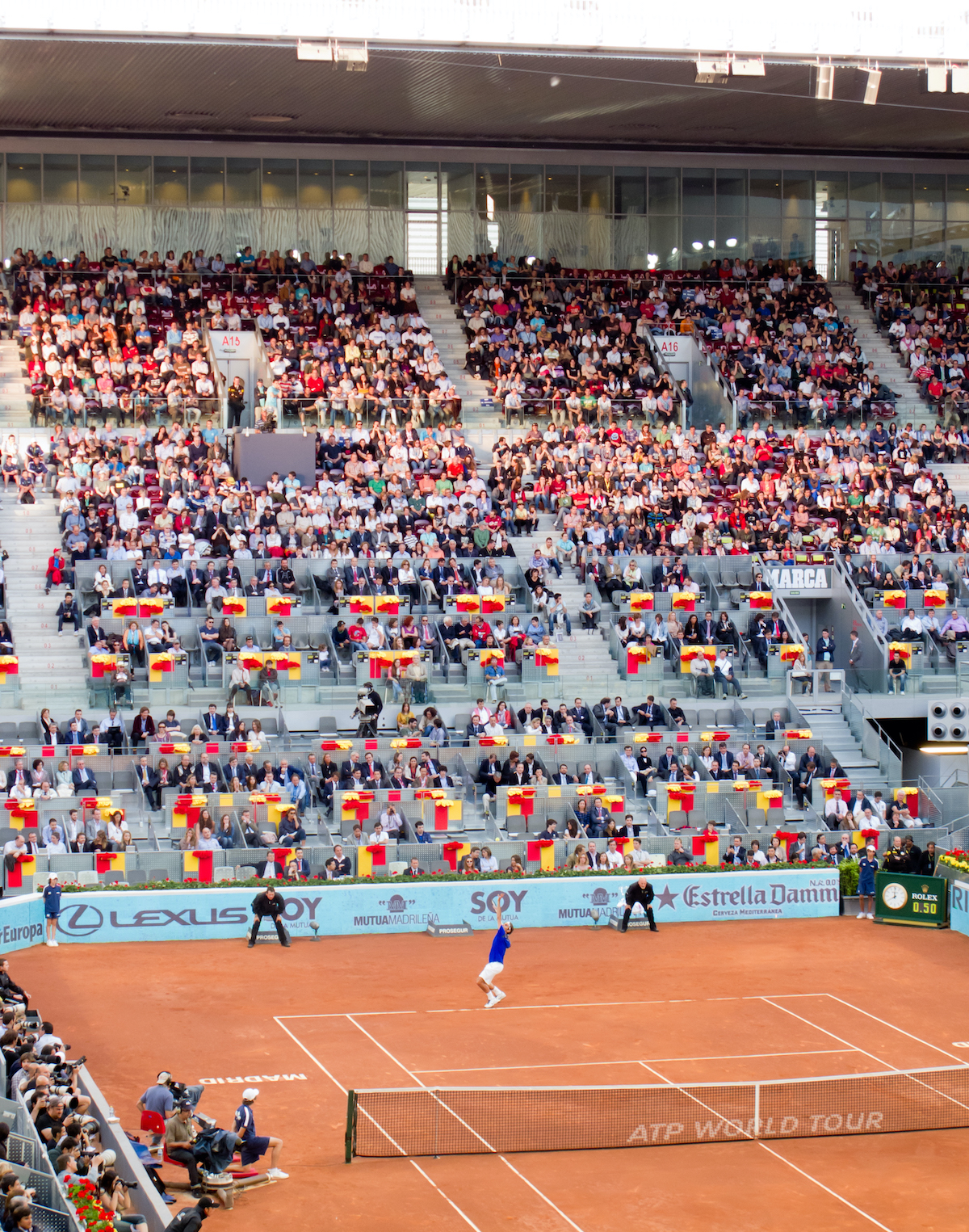 Tennis match being played on a clay court in front of a crowd.